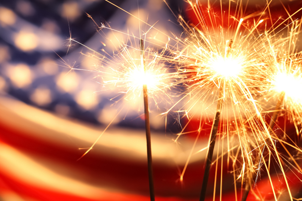 Sparklers glowing brightly in front of a blurred American flag, symbolizing Independence Day celebrations and fireworks safety.
