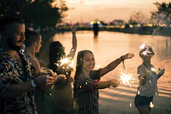 Adults with sparklers near a pond at dusk