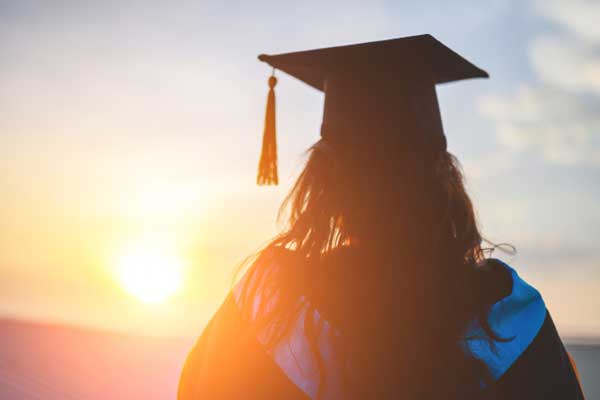 Woman from behind at sunset with graduation cap and gown
