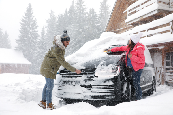 happy couple clearing off snow covered car