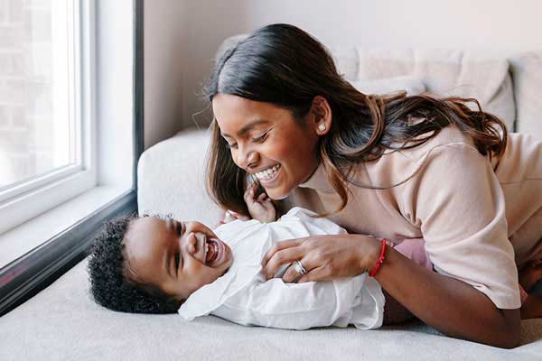 African American mother teasing baby on bed