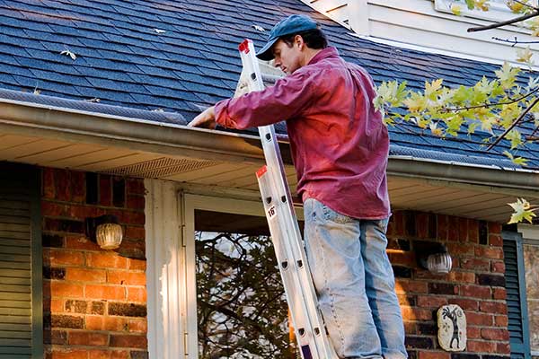 Man on ladder cleaning gutters