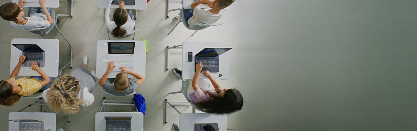 Overhead view of a teacher assisting students working at desks in a classroom.