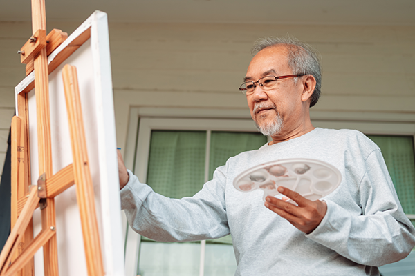 Asian senior man painting with easle