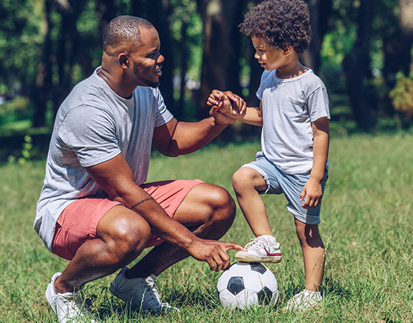 African American dad and son outside playing soccer