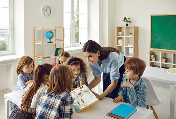 Female teacher in the classroom with a book in her hands teaches young students.